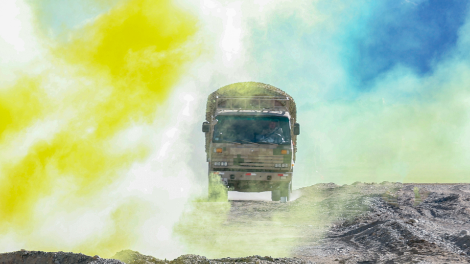 Military trucks drive through smoke and dust