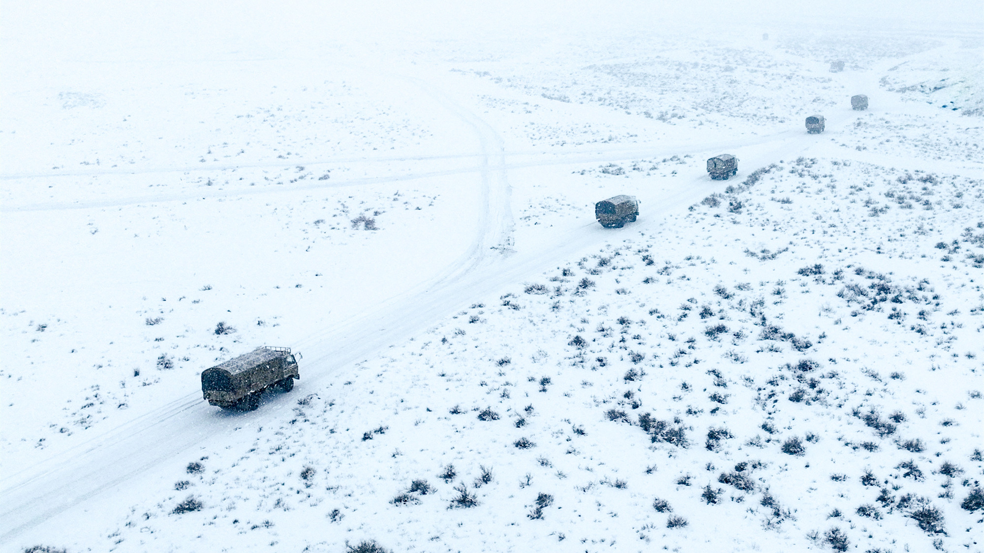 Military trucks maneuver in snowfield