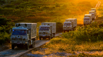 Military trucks maneuver in field 